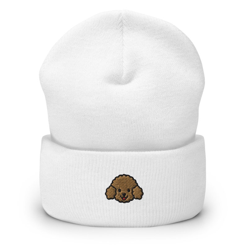 Puede incluir: Gorro de punto blanco con una cara de caniche bordada en marr&oacute;n.