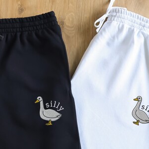 May include: Two pairs of sweatpants, one black and one white, with an embroidered goose and the word "silly" on the leg.
