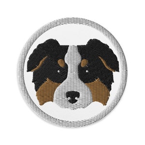 May include: Embroidered patch of an Australian Shepherd dog's face with black, brown, and white fur. The dog is looking directly at the viewer.