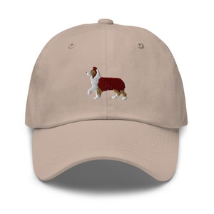 May include: A beige baseball cap with an embroidered image of an Australian Shepherd dog. The dog is standing in profile, facing to the right, with a red and white coat.