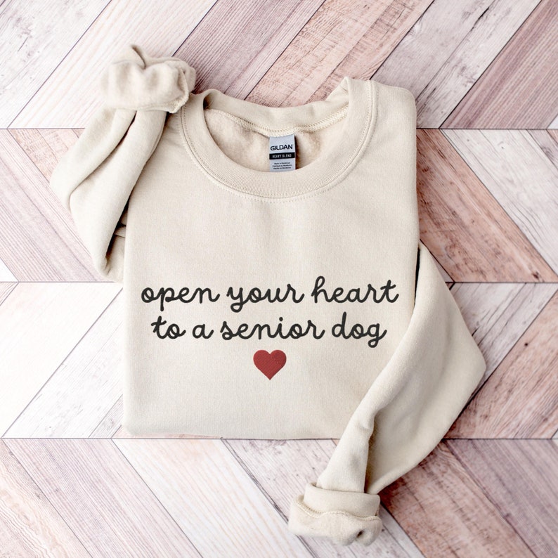 May include: A beige sweatshirt with the text "open your heart to a senior dog" and a red heart printed on the front.