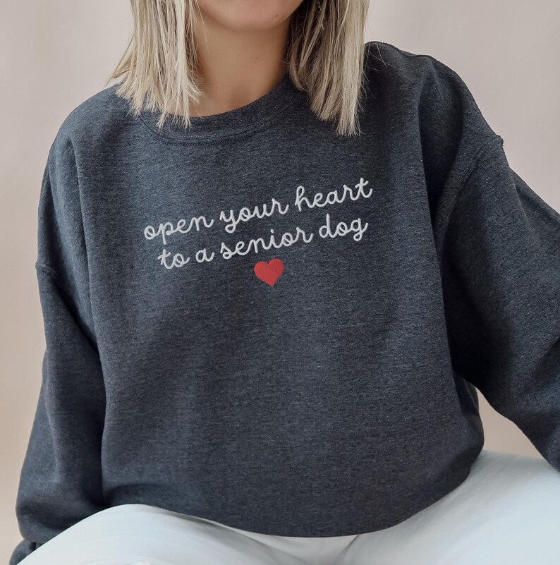 May include: A dark gray sweatshirt with the text "open your heart to a senior dog" in white lettering and a red heart.