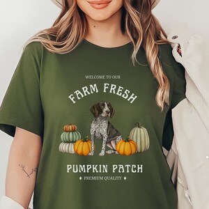 May include: Green t-shirt with a white graphic design featuring a German Shorthaired Pointer dog sitting in front of pumpkins. The text reads "Welcome to our Farm Fresh Pumpkin Patch, Premium Quality".