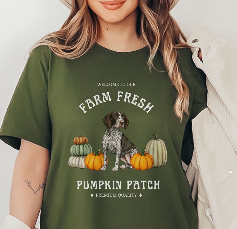 May include: Green t-shirt with a white graphic design featuring a German Shorthaired Pointer dog sitting in front of pumpkins. The text reads "Welcome to our Farm Fresh Pumpkin Patch, Premium Quality".