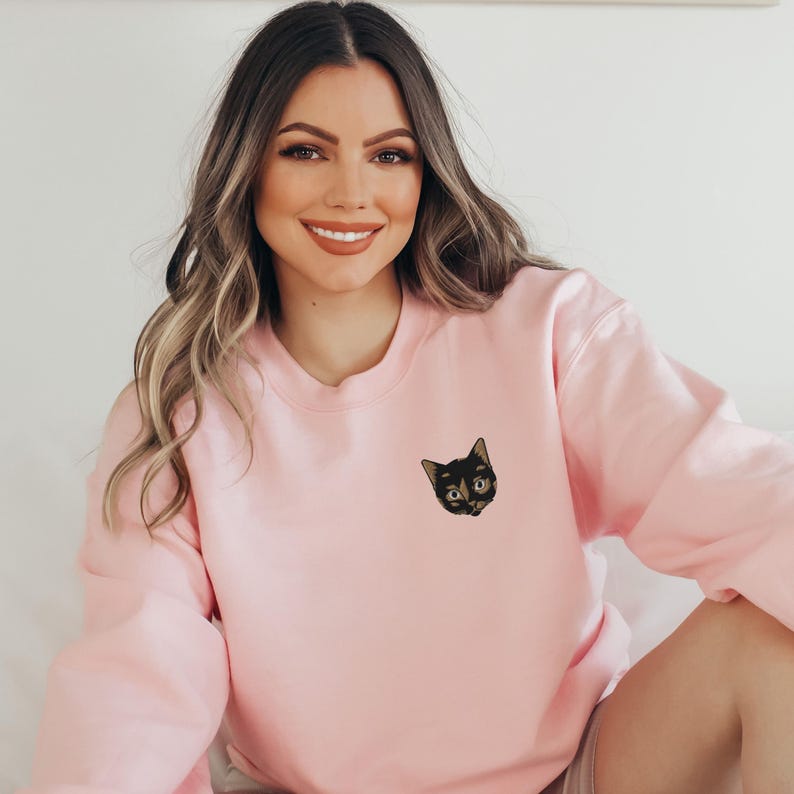 Op de afbeelding: Een roze sweatshirt met een geborduurd zwart katje op de voorkant.