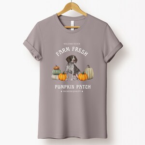 May include: A gray t-shirt with a white graphic design featuring a German Shorthaired Pointer dog sitting amongst pumpkins. The text reads "Welcome to our Farm Fresh Pumpkin Patch, Premium Quality".