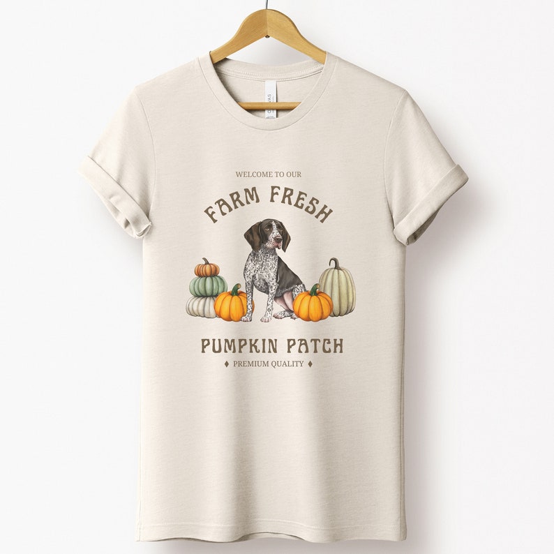 May include: A beige t-shirt with a brown graphic design featuring a dog sitting in front of pumpkins. The graphic says "Welcome to our Farm Fresh Pumpkin Patch, Premium Quality".