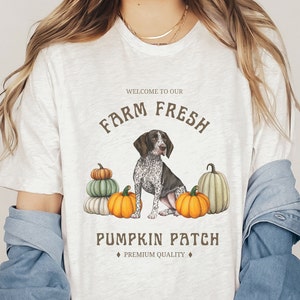 May include: White t-shirt with a brown and white dog illustration and pumpkins. The text "Welcome to our Farm Fresh Pumpkin Patch" is printed on the shirt.  "Premium Quality" is printed below the text.