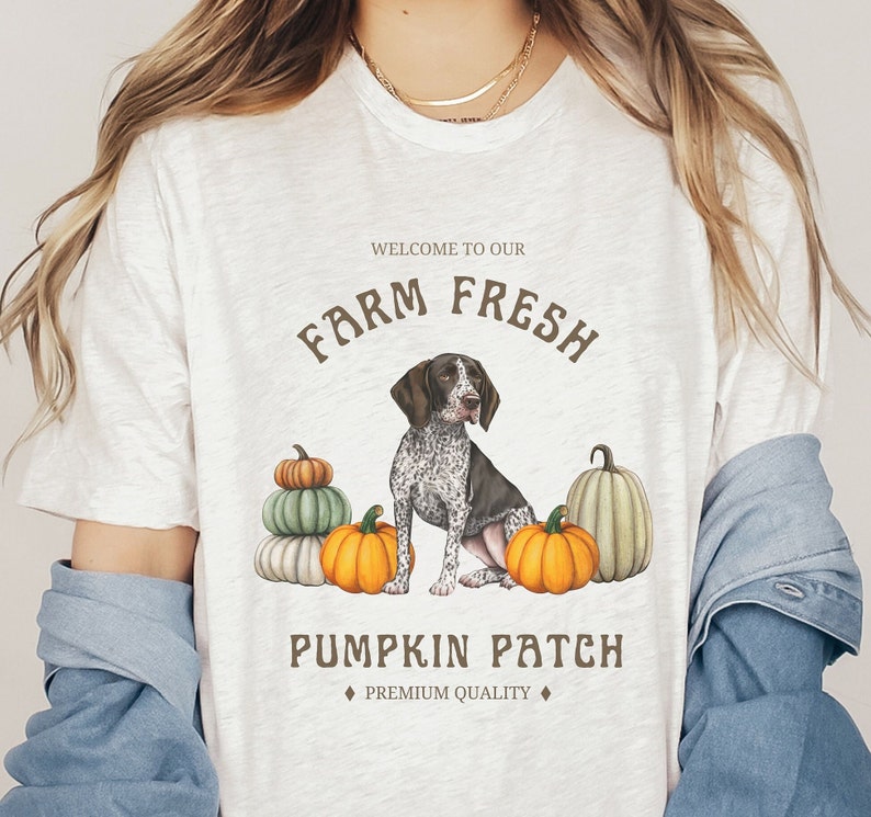 May include: White t-shirt with a brown and white dog illustration and pumpkins. The text "Welcome to our Farm Fresh Pumpkin Patch" is printed on the shirt.  "Premium Quality" is printed below the text.