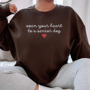 May include: A black sweatshirt with the text "open your heart to a senior dog" in white lettering and a red heart.