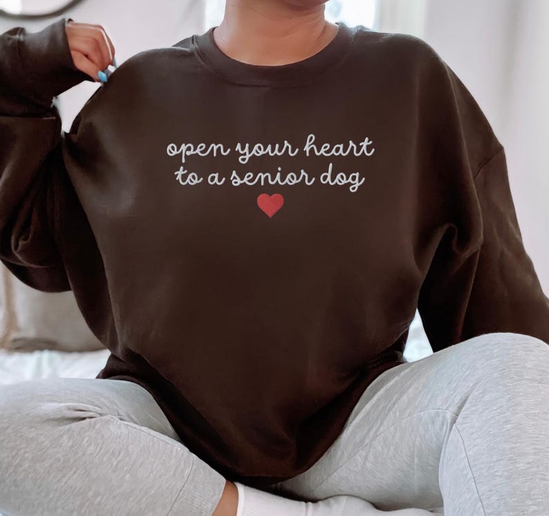 May include: A black sweatshirt with the text "open your heart to a senior dog" in white lettering and a red heart.