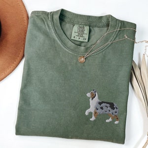 May include: A green t-shirt with an embroidered image of an Australian Shepherd dog. The shirt has a tag that says "Comfort Colors" and "S - P - CH".