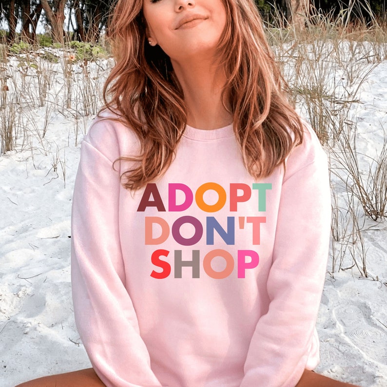 May include: Pink sweatshirt with the text "ADOPT DON'T SHOP" in colorful letters.