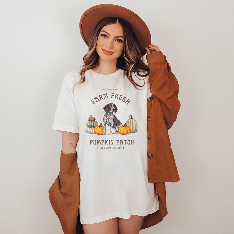 May include: White t-shirt with a graphic design of a dog sitting in front of pumpkins. The text on the shirt reads "Welcome to our Farm Fresh Pumpkin Patch, Premium Quality".