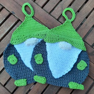 Könnte beinhalten: Zwei gehäkelte Topflappen in Form von Gnomen mit grünen Hüten, weißen Bärten und grauen Körpern. Die Gnome haben grüne Akzente an ihren Hüten und Körpern.