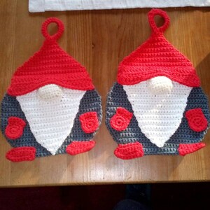 Könnte beinhalten: Zwei gehäkelte Gnomen-Topflappen mit roten Mützen, weißen Bärten, grauen Körpern und roten Fäustlingen.