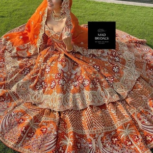 Puede incluir: Un vestido de novia naranja con intrincados bordados y adornos. El vestido presenta patrones florales y geom&eacute;tricos, con una falda en capas y un velo a juego. El texto "MAD BRIDALS WE MAKE YOU WEAR THE BEST" es visible.