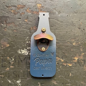 May include: A blue wooden bottle opener shaped like a beer bottle with a copper bottle opener. The bottle opener has the text "Bester Papa der Welt!" engraved on it.