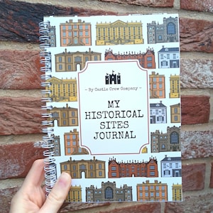 May include: A spiral-bound journal with a white cover featuring a repeating pattern of colourful historical buildings. The centre label displays a black castle icon, the text "By Castle Crew Company," and the title "MY HISTORICAL SITES JOURNAL."