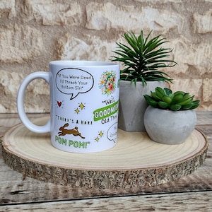 May include: White ceramic mug with a colourful cartoon design featuring a hare, a speech bubble with the text "There's a hare Pom Pom!" and another speech bubble with the text "If you were dead I'd thrash your bottom sir!"