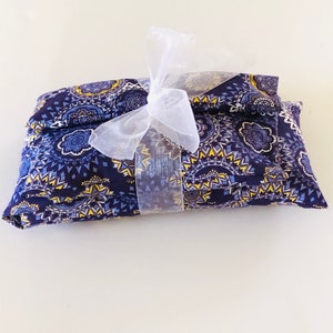 May include: A navy blue fabric item with a yellow and white geometric pattern is tied with a sheer white ribbon. The fabric is folded and appears to be a pillow or a similar item. The background is white.