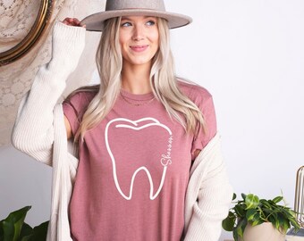 May include: A mauve t-shirt with a white outline of a tooth and the name "Shannon" written inside the tooth.