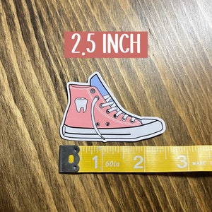 May include: Pink and blue high-top sneaker with a white tooth graphic. The sticker is 2.5 inches tall.