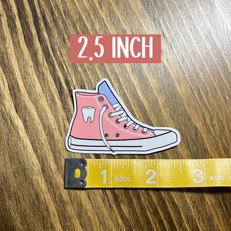 May include: Pink and blue high-top sneaker with a white tooth graphic. The sticker is 2.5 inches tall.