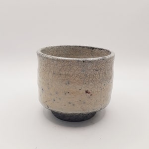 May include: A white ceramic teacup with a crackled glaze and a dark grey base.