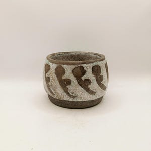 May include: A small, round ceramic planter with a textured, crackled white glaze finish. The exterior features a repeating pattern of dark brown, abstract, curved brushstroke shapes encircling the middle. The base and rim are dark brown.