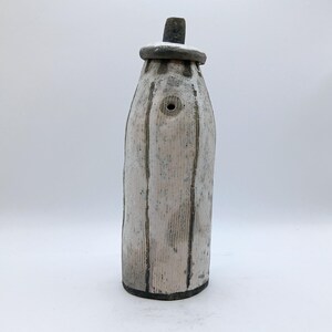 May include: A white ceramic bottle with a textured surface and a black lid. The bottle has a small hole near the top.