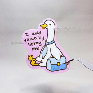 May include: A sticker featuring a cartoon goose with a blue tie and briefcase, sitting on a pink background. The text "I add value by being me" is written on the sticker. The goose has a yellow beak and feet.
