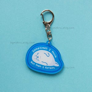 May include: A blue acrylic keychain with a silver clasp. The keychain features a white seal illustration and the text "Sometimes I think But then I forget". The background is a solid light blue.