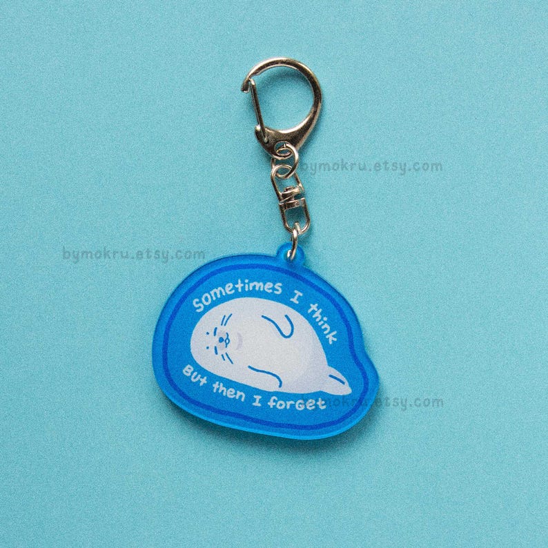 May include: A blue acrylic keychain with a silver clasp. The keychain features a white seal illustration and the text "Sometimes I think But then I forget". The background is a solid light blue.