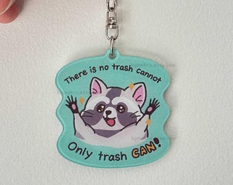 Könnte beinhalten: Ein türkisfarbener Acryl-Schlüsselanhänger mit einem Cartoon-Waschbären mit erhobenen Pfoten. Der Text lautet: There is no trash cannot Only trash CAN! Das Design enthält kleine gelbe Sternakzente und einen silbernen Karabinerhaken.