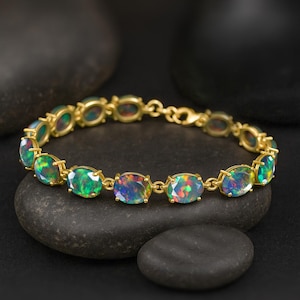 May include: A gold bracelet featuring oval-cut opals. The opals display a vibrant play of color, with flashes of green, blue, and red. The bracelet is set on a dark background, highlighting the gemstones.