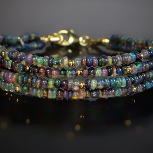 May include: A multi-strand bracelet made of black opal beads with gold accents. The bracelet is made of four strands of beads and has a gold clasp.