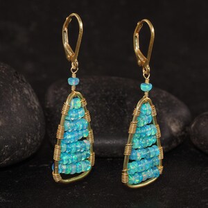 K&ouml;nnte beinhalten: Ein Paar goldfarbene Ohrringe mit Tropfendesign. Die Ohrringe haben Reihen aus kleinen, hellblauen Perlen, die in einem goldfarbenen Drahtrahmen eingeschlossen sind. Die Ohrringe haben einen B&uuml;gelverschluss und eine kleine blaue Perle oben.