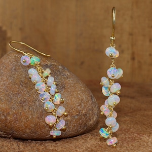 Könnte beinhalten: Ein Paar goldene Ohrringe mit weißen, schillernden Opalperlen. Die Ohrringe hängen an einem Stein.