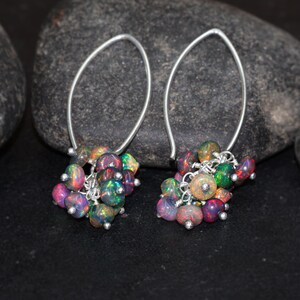 May include: A pair of silver dangle earrings with a cluster of iridescent opal beads. The beads are a mix of pink, green, and black.