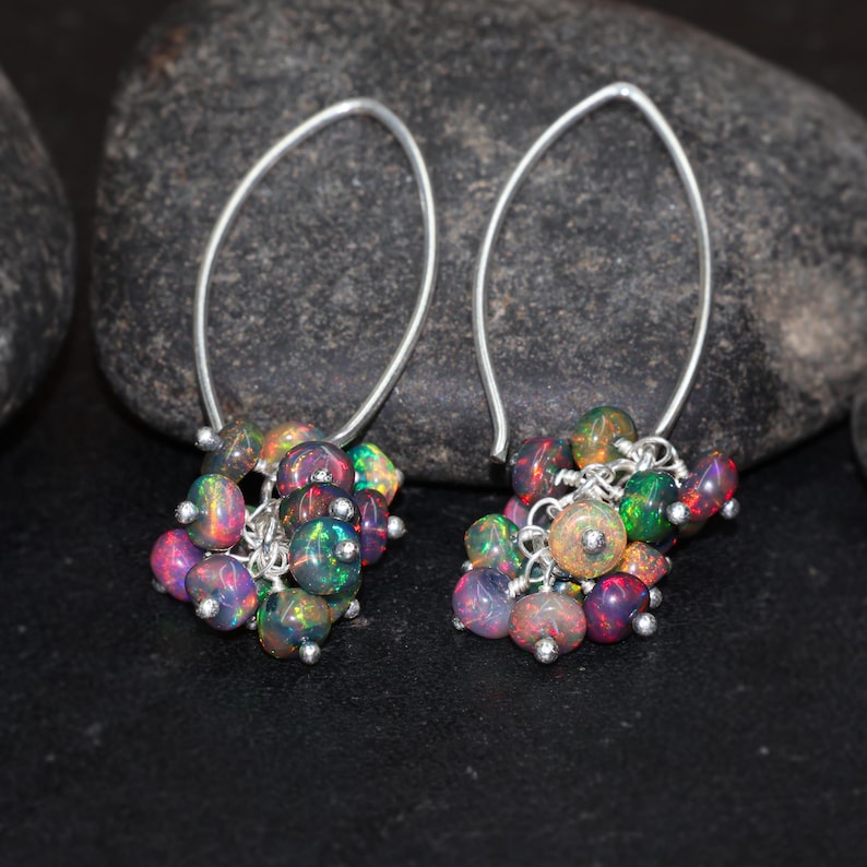 May include: A pair of silver dangle earrings with a cluster of iridescent opal beads. The beads are a mix of pink, green, and black.