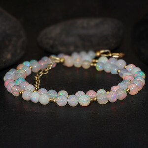 May include: A double strand necklace made with white opal beads and gold spacers. The necklace is on a dark background.