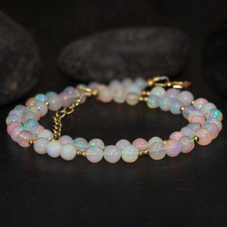 May include: A double strand necklace made with white opal beads and gold spacers. The necklace is on a dark background.