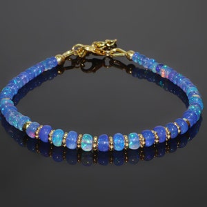 May include: A delicate bracelet made with blue opal beads and gold accents. The bracelet is made with small, round beads and has a simple clasp.