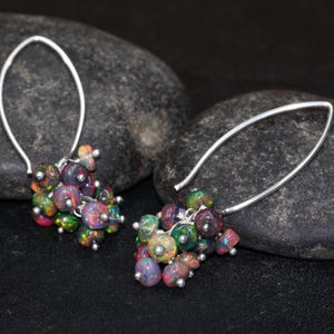 May include: A pair of silver dangle earrings with a cluster of iridescent opal beads. The earrings are made of a thin silver wire and have a simple, elegant design.