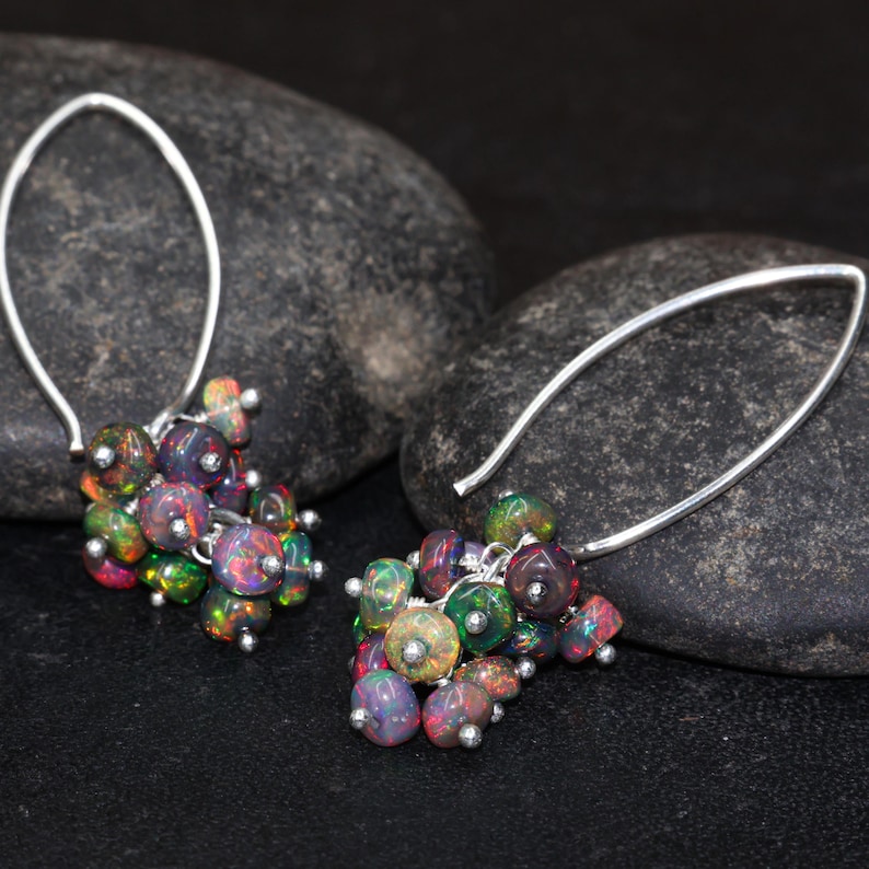 May include: A pair of silver dangle earrings with a cluster of iridescent opal beads. The earrings are made of a thin silver wire and have a simple, elegant design.