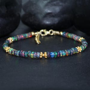 May include: A delicate bracelet made with a strand of iridescent black opal beads interspersed with tiny gold beads. The bracelet has a simple clasp closure.