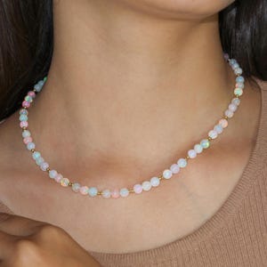 May include: A delicate necklace made of small, iridescent opal beads strung on a gold chain. The necklace is a simple and elegant design, perfect for everyday wear.