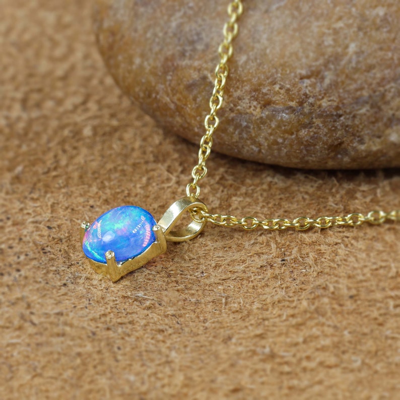 May include: A gold chain necklace with a blue opal pendant. The opal is set in a gold bezel and has a delicate, iridescent shimmer.