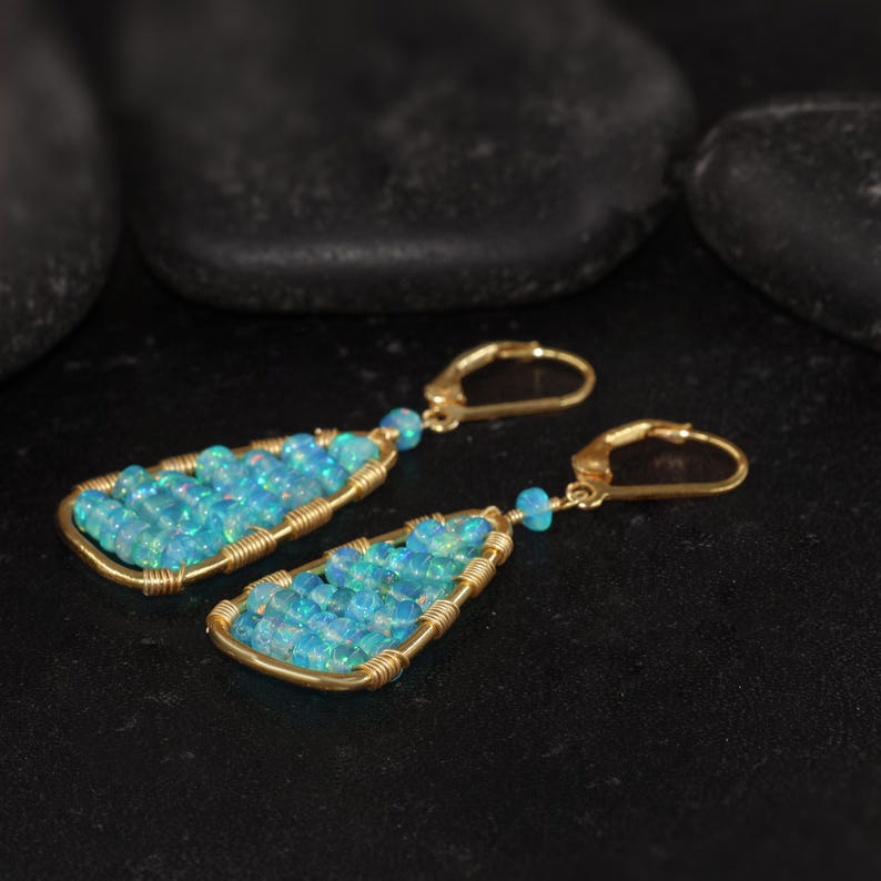 K&ouml;nnte beinhalten: Ein Paar goldfarbene, drahtgewickelte Ohrringe. Jeder Ohrring hat ein tropfenf&ouml;rmiges Design, das mit kleinen, hellblauen Opalsteinen gef&uuml;llt ist. Die Ohrringe haben einen Klappb&uuml;gelverschluss.